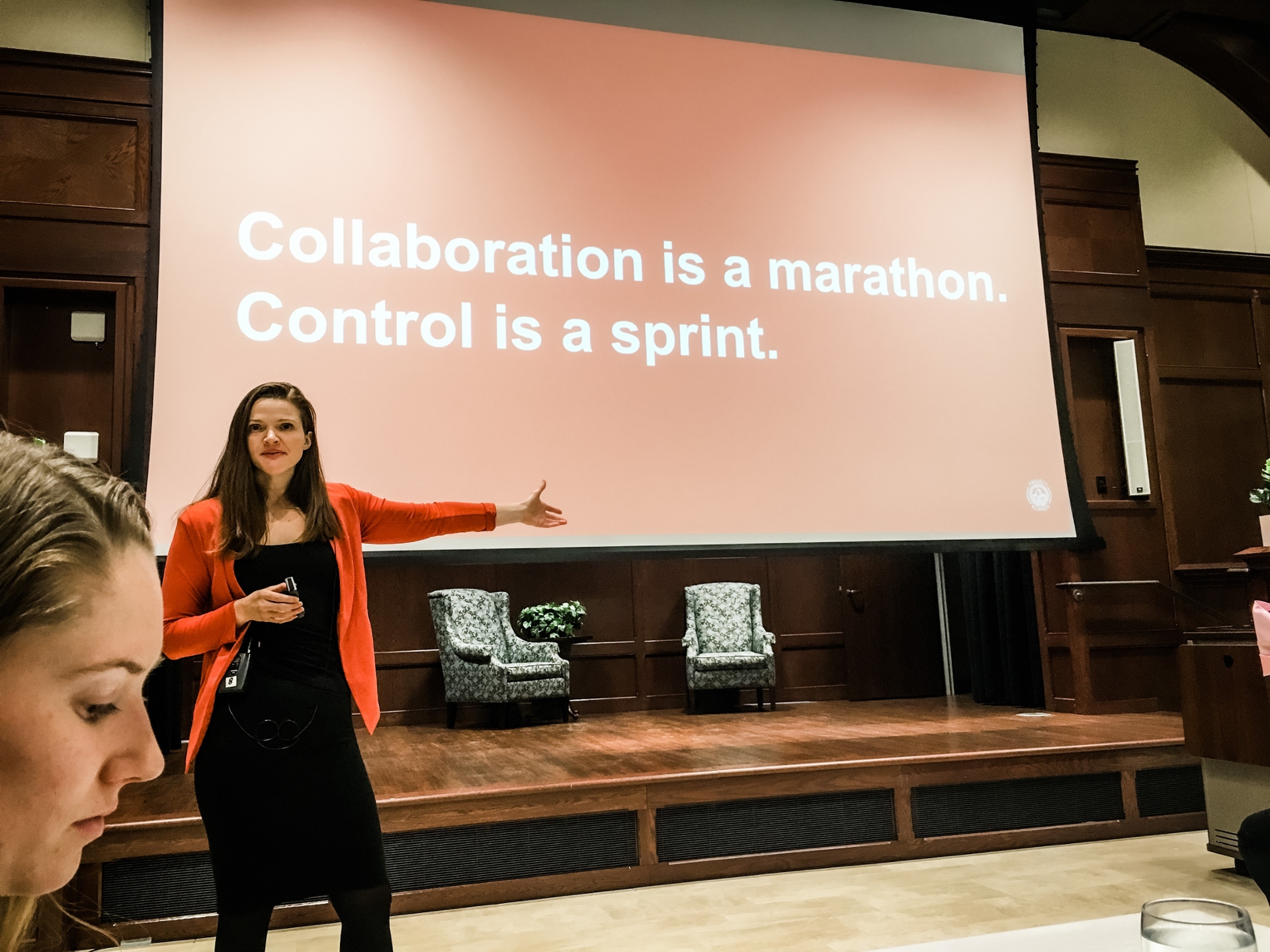 Kristin van Busum speaking at a Women's Leadership event, with a screen in the background that reads "Collaboration is a marathon. Control is a sprint."