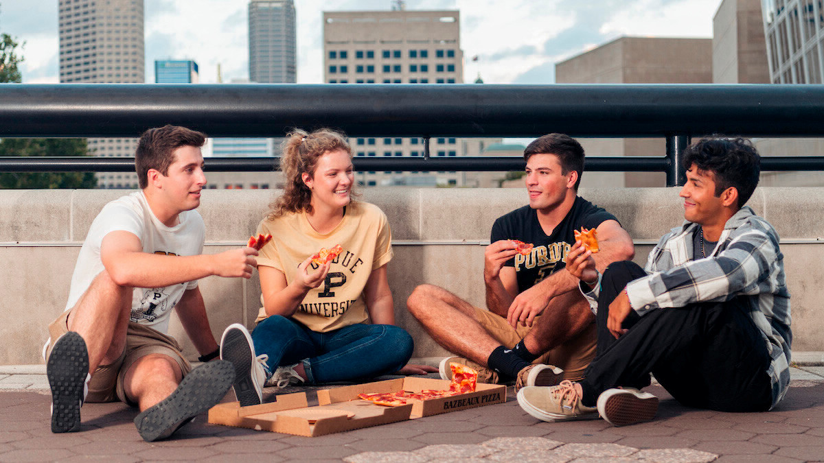 A group of students sitting, talking, and eating pizza.