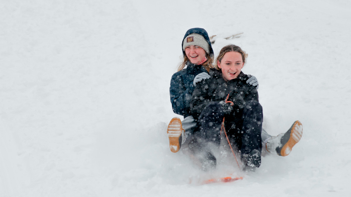 Two students sledding down Slayter Hill.