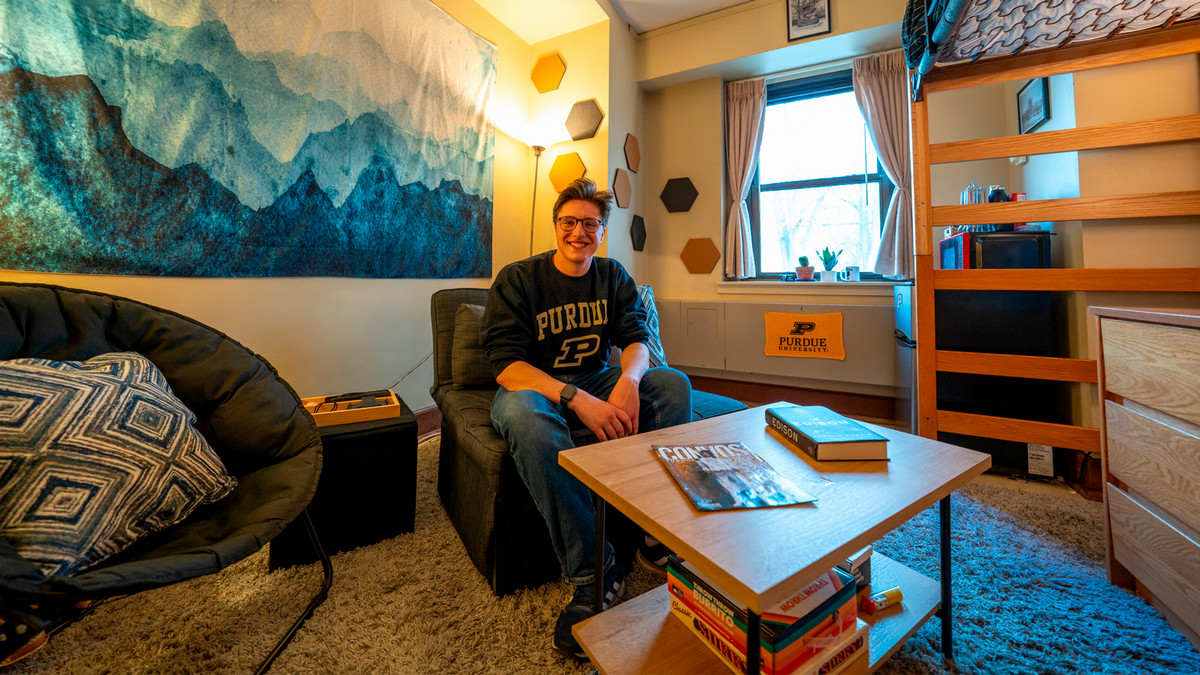 Student in his dorm room with a lofted bed.