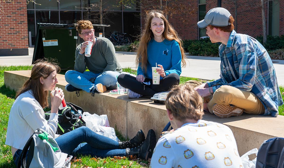 University Residents enjoying a beverage outside on the benches located on the Krach lawn. 