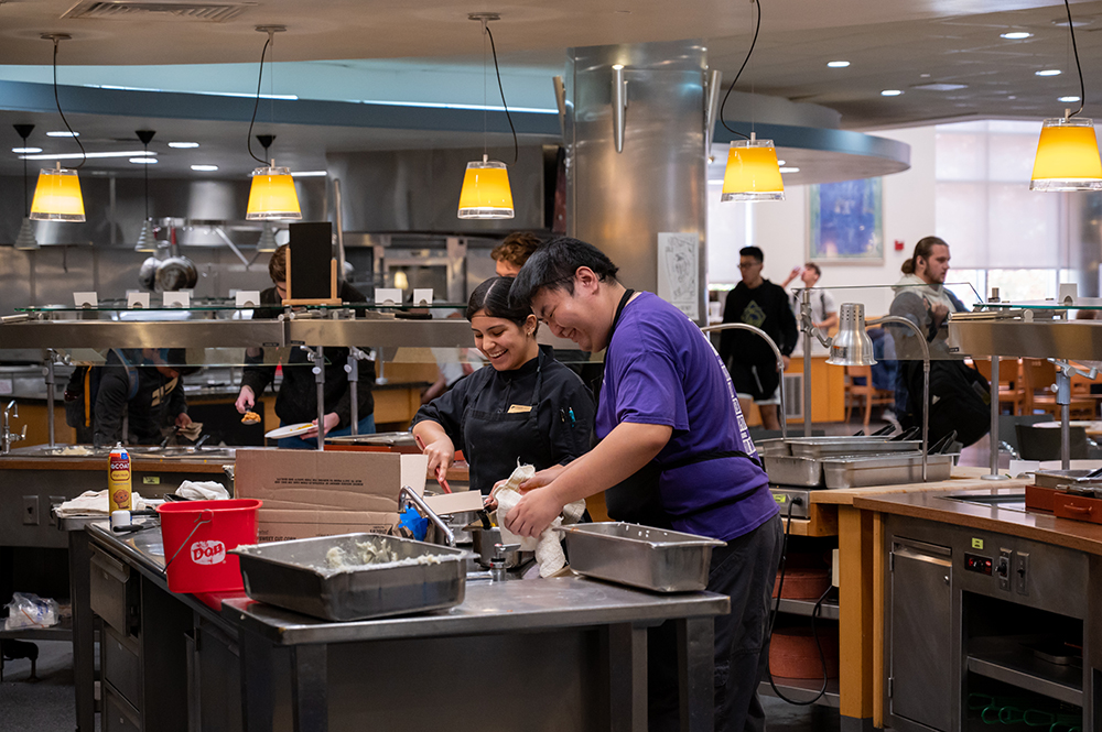 Dining employees smile while preparing food in Ford Dining Court.