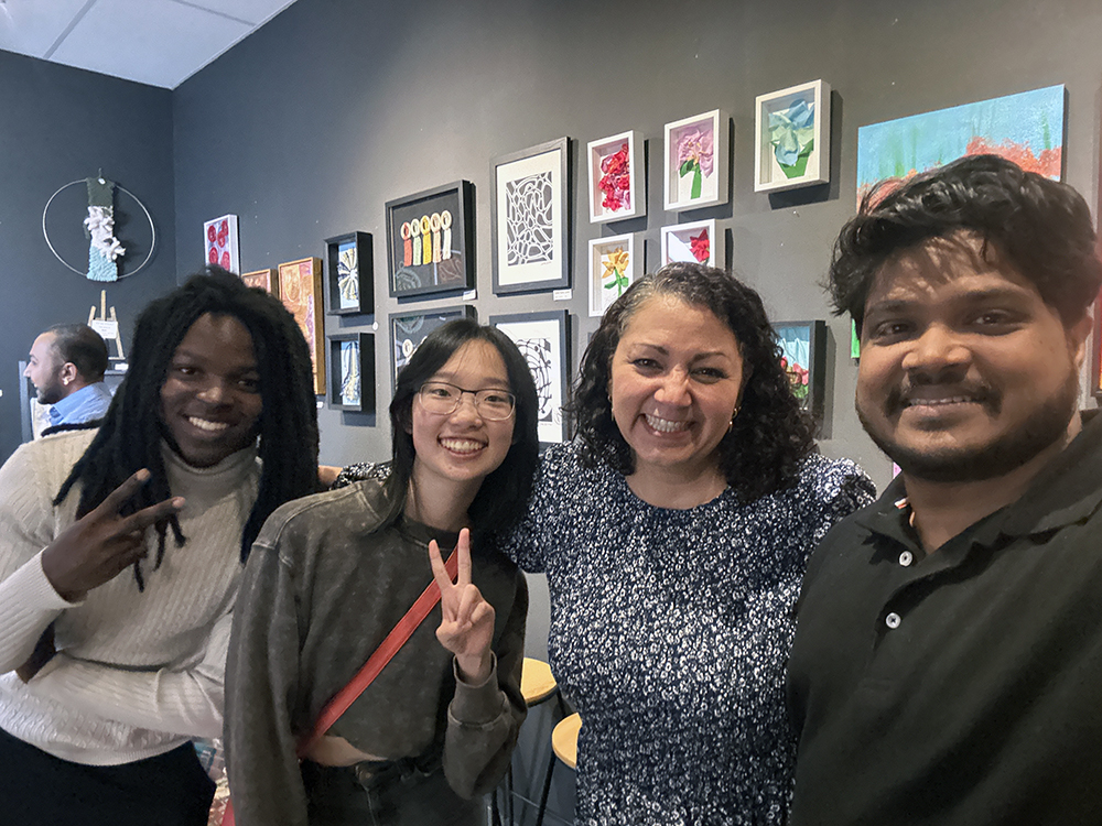 People posing in front of colorful artwork hanging on a wall.